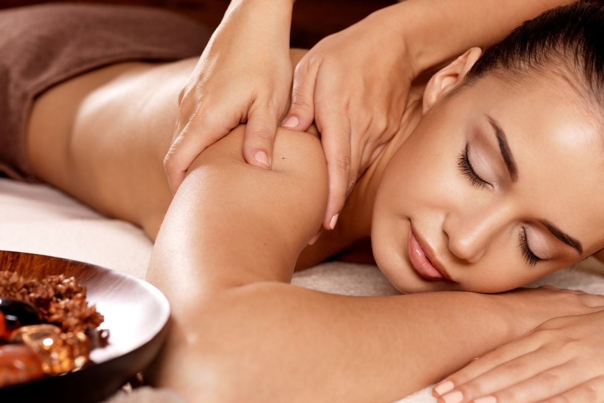 Guest resting with eyes closed while a therapist applies acupressure across the shoulder during a back rub
