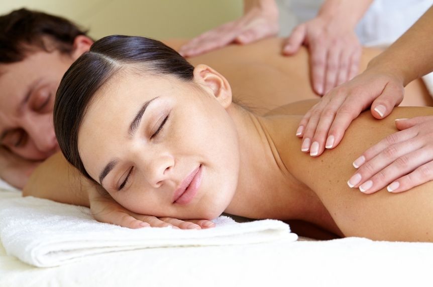 Two guests lying side by side on adjacent tables while therapists work across their backs and shoulders