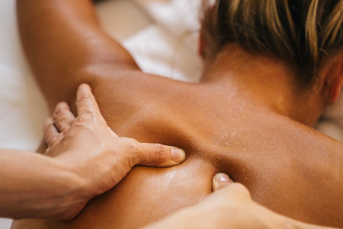 Therapist using thumbs and palms to work out tension along a guest's upper back during a back rub in New York City