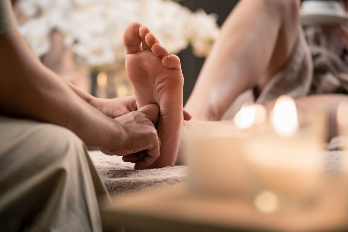 Therapist pressing the arch of a guest's foot with candles and white orchids in the background